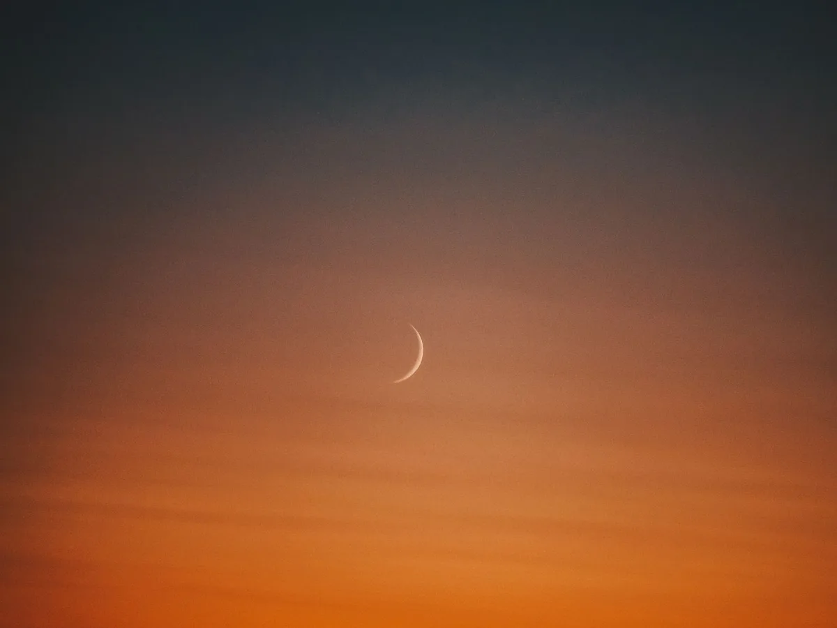 A serene crescent moon set against a warm, gradient twilight sky.