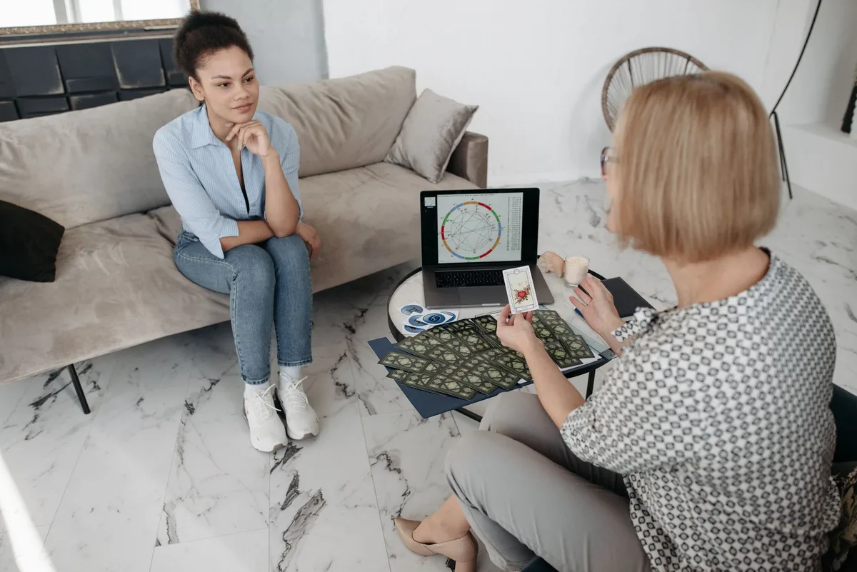 Women discuss astrology with a natal chart and tarot cards on a couch.