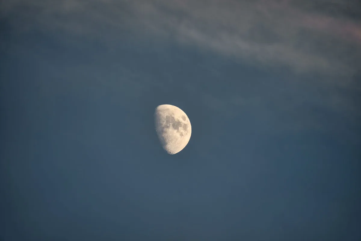 A serene half moon set against a partially cloudy night sky, creating a tranquil celestial scene.