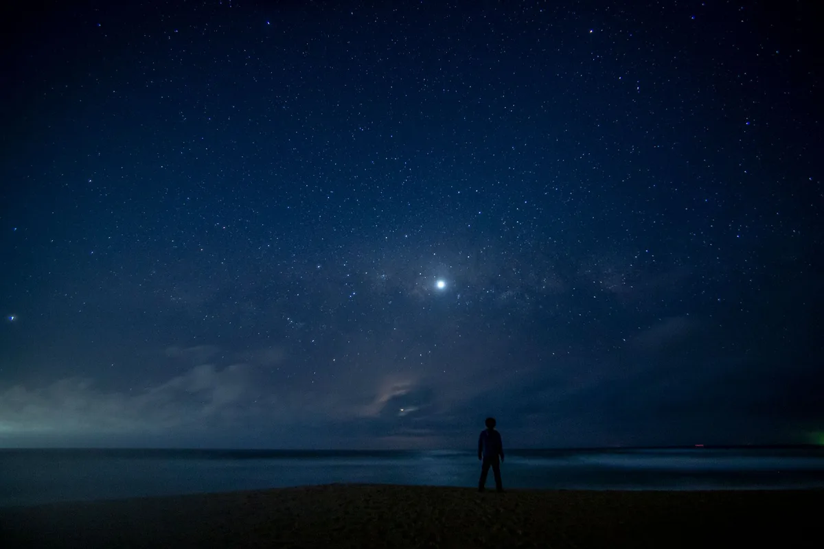 A lone figure stands under a vast starry night sky on a beach in Tunquen, Chile.