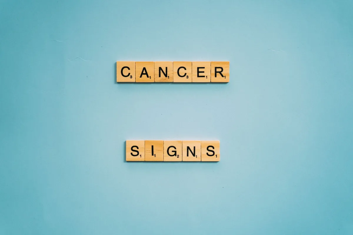 Wooden letter tiles spelling 'Cancer Signs' on a blue background for health awareness.