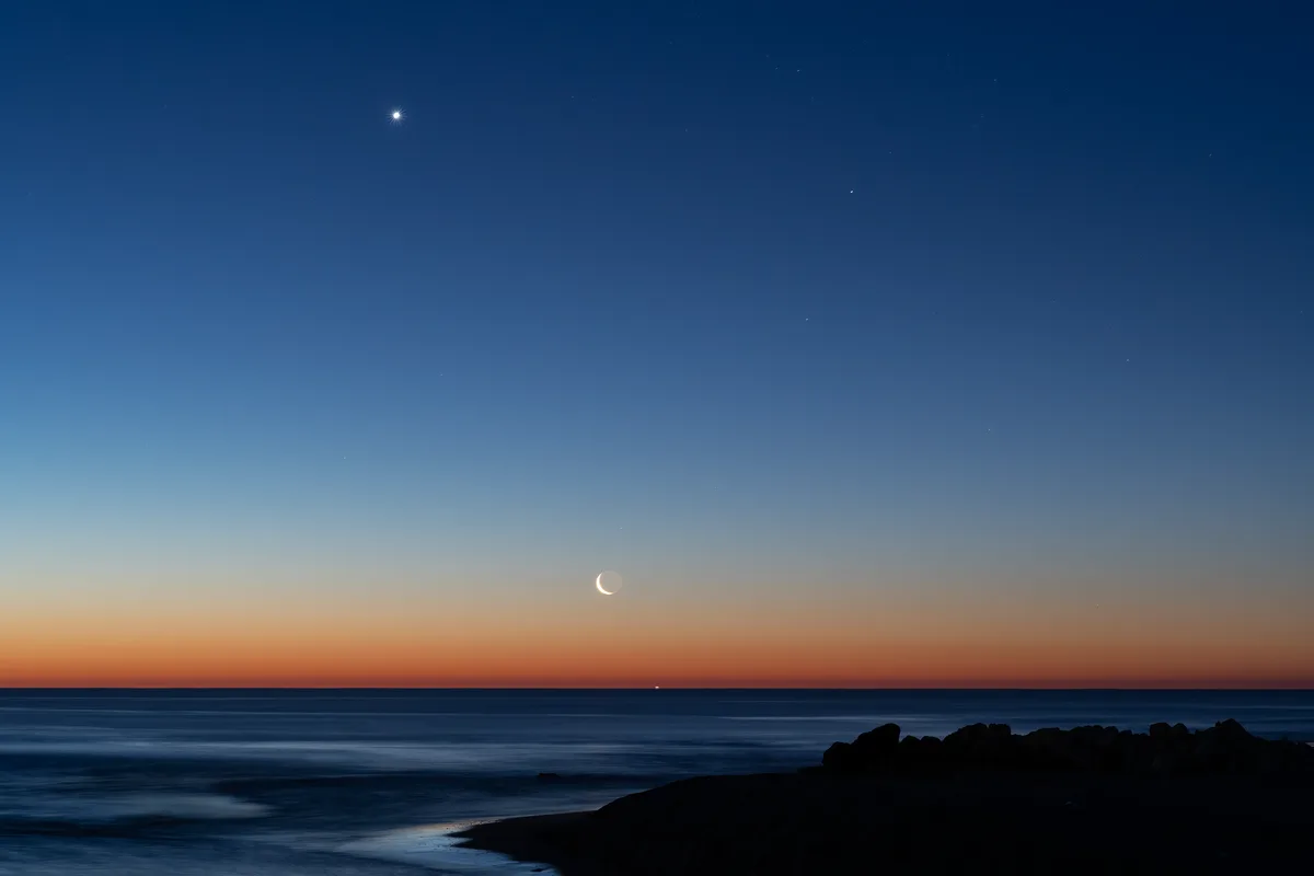 Captivating view of crescent moon and planets aligning over the ocean at twilight near Valencia, Spain.